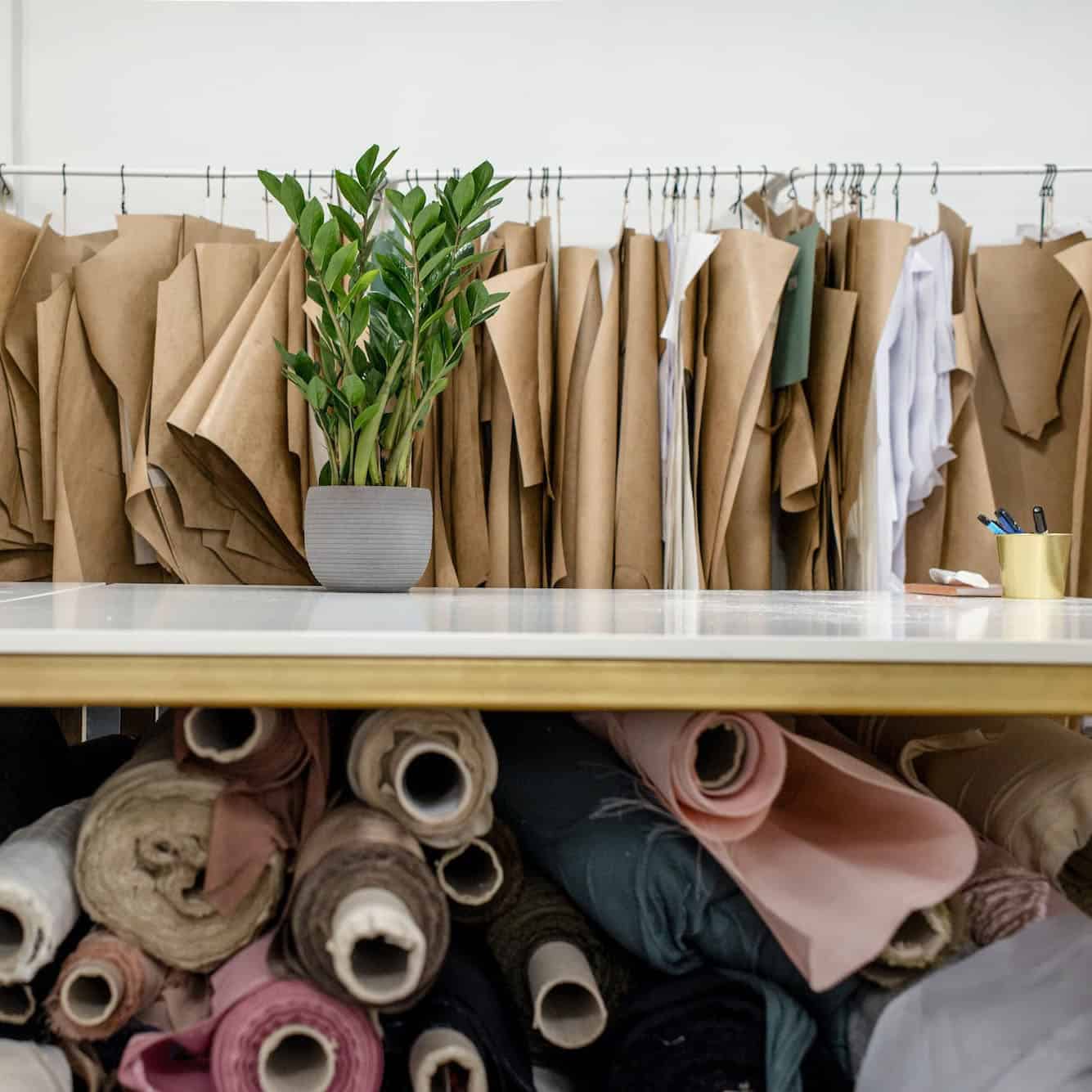 desk with rolls of fabric stacked under it, and fabric pieces hanging on a rack behind